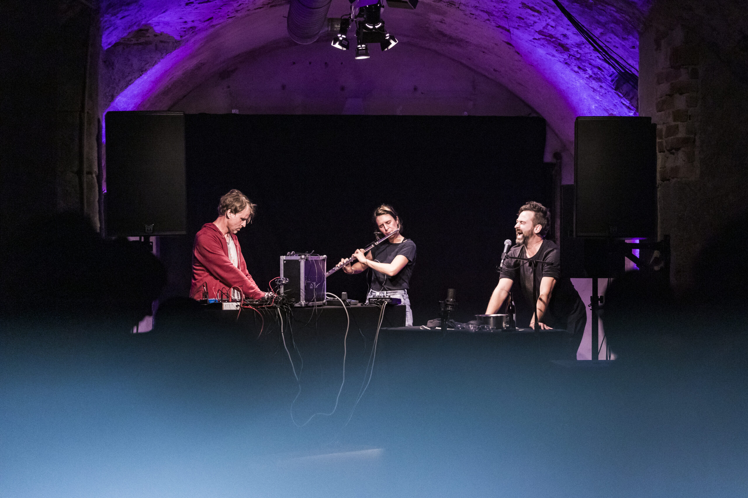Die Band - zu dritt - im Live-Setting. Dunkler Raum.